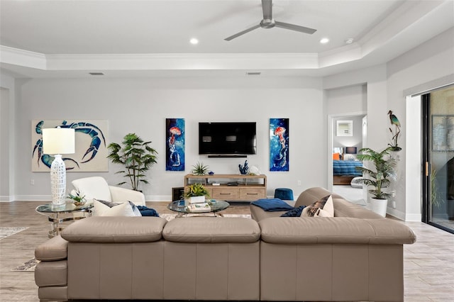 living room featuring light hardwood / wood-style flooring, a tray ceiling, crown molding, and ceiling fan