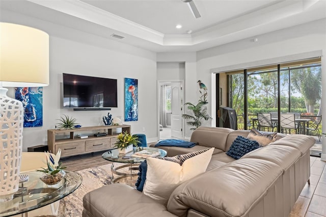 living room featuring ceiling fan, a tray ceiling, and light wood-type flooring