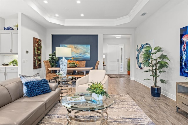 living room featuring crown molding, light wood-type flooring, and a raised ceiling