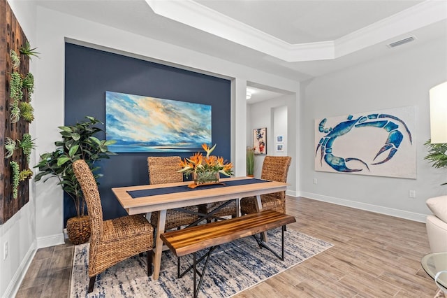 dining area with a raised ceiling, ornamental molding, and hardwood / wood-style floors