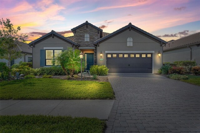 26810 Weiskopf Dr, Englewood, FL 34223 - view of front of home featuring a garage, decorative driveway, a front lawn, stone siding, and stucco siding