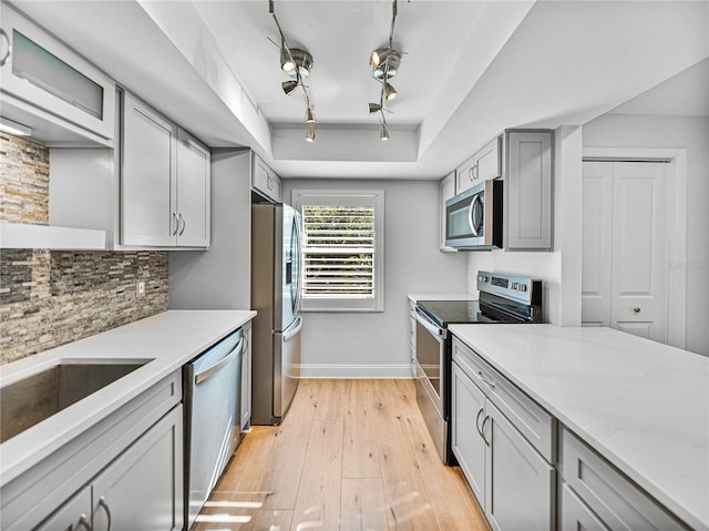 kitchen with gray cabinetry, light stone countertops, tasteful backsplash, light hardwood / wood-style floors, and appliances with stainless steel finishes