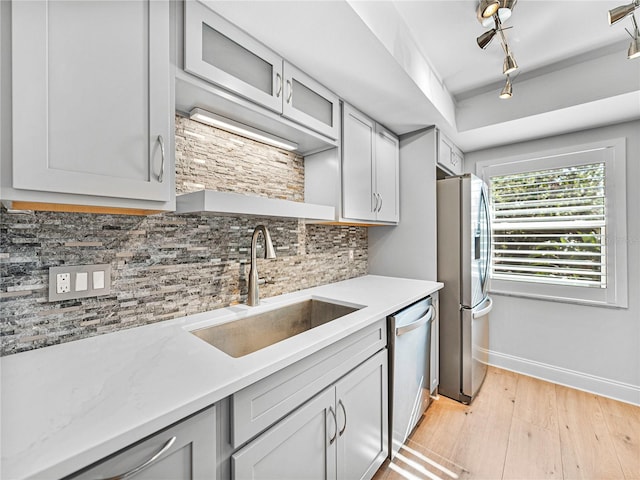 kitchen with decorative backsplash, rail lighting, stainless steel appliances, sink, and light hardwood / wood-style floors