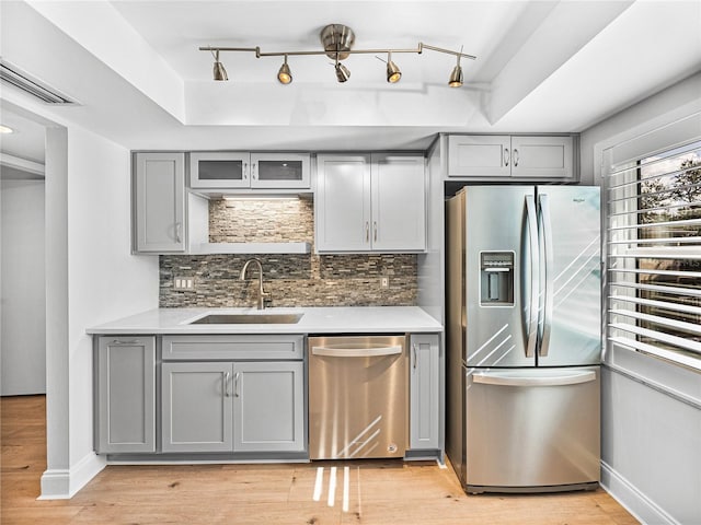 kitchen with sink, a raised ceiling, light hardwood / wood-style floors, gray cabinets, and appliances with stainless steel finishes