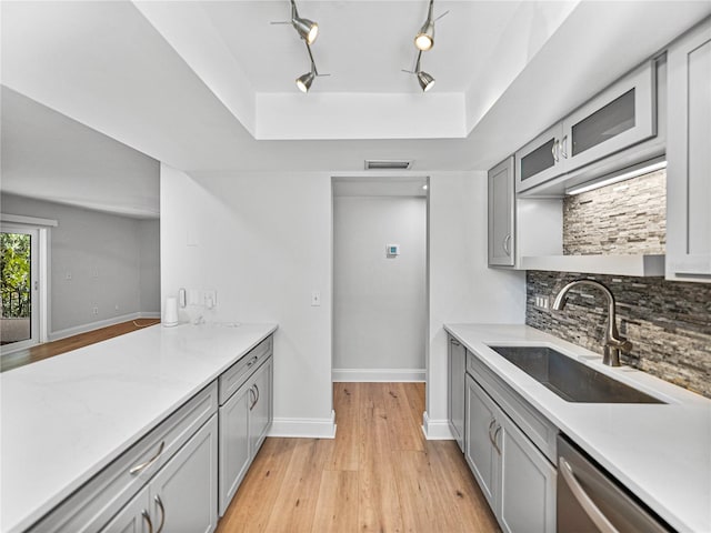 kitchen with dishwasher, a raised ceiling, sink, gray cabinets, and light hardwood / wood-style floors