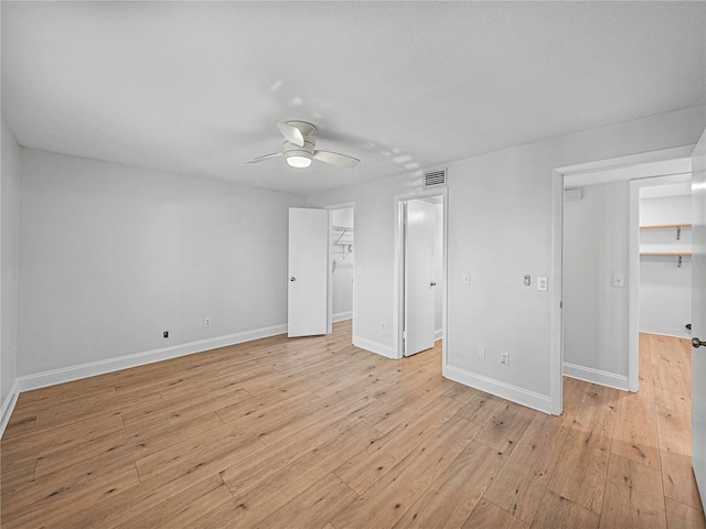 unfurnished bedroom with a walk in closet, ceiling fan, a closet, and light wood-type flooring