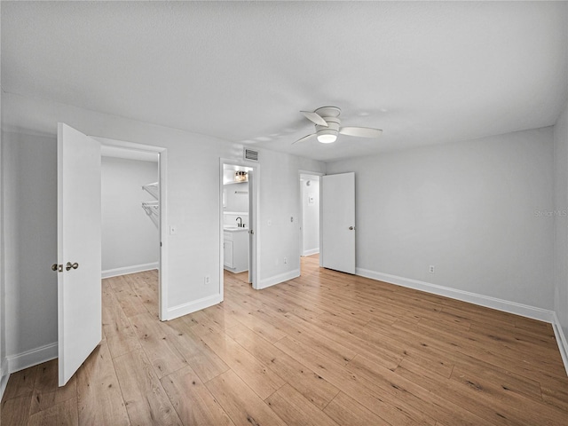 unfurnished bedroom featuring a walk in closet, sink, ceiling fan, light wood-type flooring, and a closet