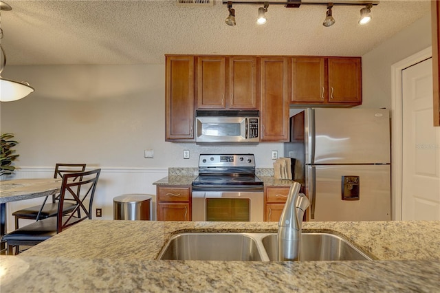 kitchen with sink, a textured ceiling, stainless steel appliances, light stone counters, and track lighting