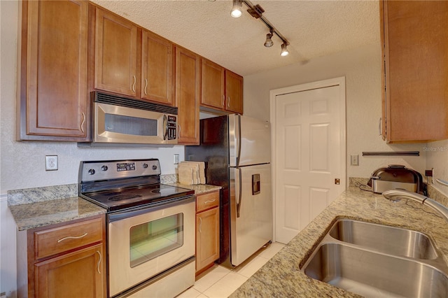 kitchen with track lighting, sink, light tile patterned flooring, appliances with stainless steel finishes, and a textured ceiling