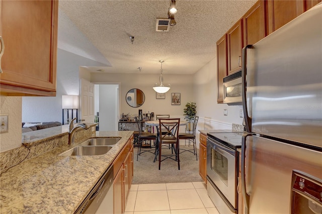 kitchen with sink, a textured ceiling, stainless steel appliances, pendant lighting, and light tile patterned floors