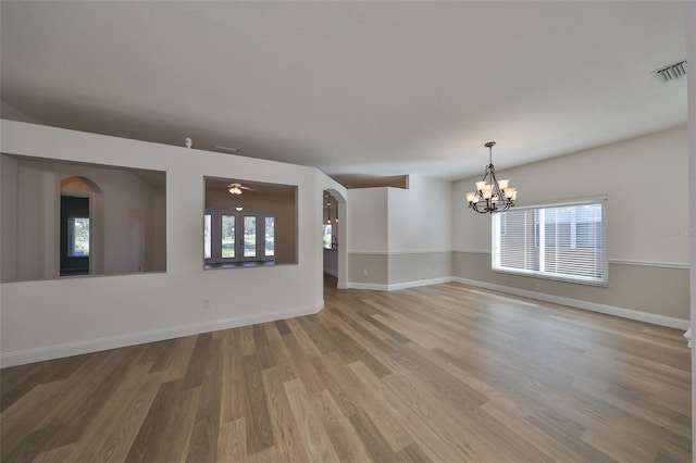 unfurnished room with hardwood / wood-style flooring, ceiling fan with notable chandelier, and plenty of natural light