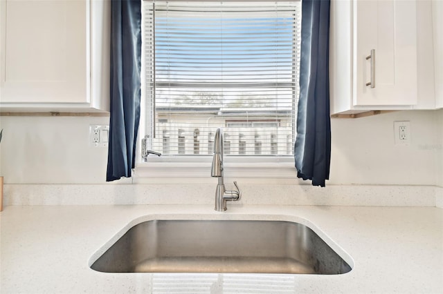 room details with white cabinetry, light stone countertops, and sink