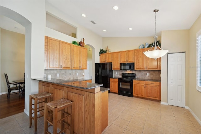 kitchen with kitchen peninsula, decorative backsplash, dark stone counters, black appliances, and decorative light fixtures