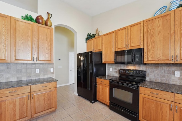 kitchen with dark stone countertops, black appliances, light tile patterned floors, and decorative backsplash