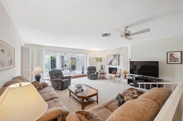 living room featuring a textured ceiling, light colored carpet, ceiling fan, and a tiled fireplace