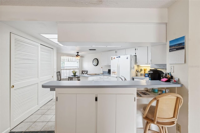 kitchen with a kitchen breakfast bar, white cabinets, kitchen peninsula, and white refrigerator with ice dispenser