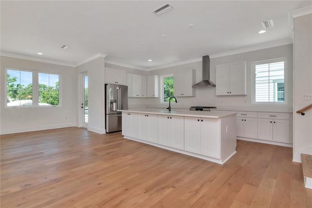kitchen featuring visible vents, wall chimney range hood, light countertops, white cabinetry, and high end refrigerator