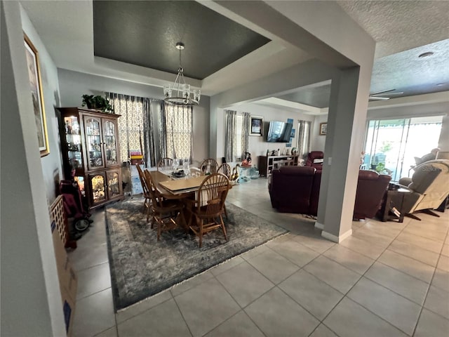 dining area with a notable chandelier, a textured ceiling, a tray ceiling, and light tile patterned floors