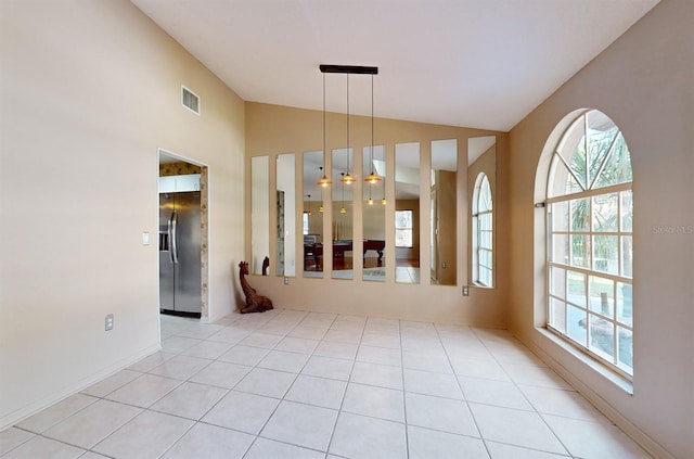 spare room featuring vaulted ceiling, light tile patterned floors, and plenty of natural light