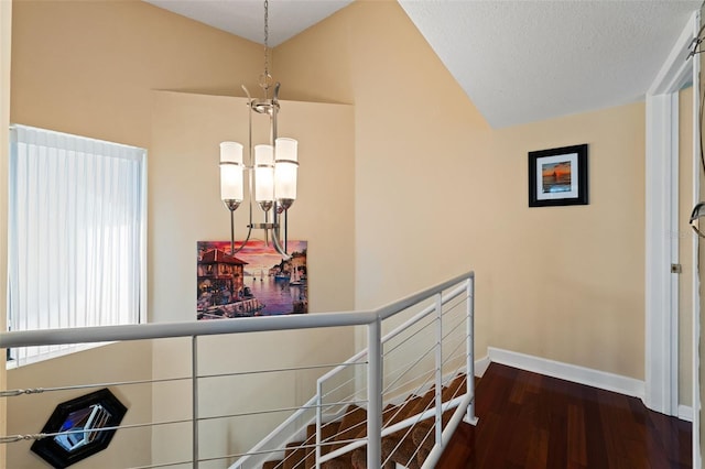 corridor featuring a chandelier, a textured ceiling, dark wood-type flooring, and lofted ceiling