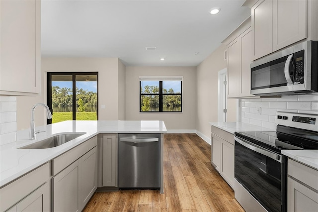 kitchen featuring decorative backsplash, appliances with stainless steel finishes, light stone countertops, light hardwood / wood-style floors, and sink