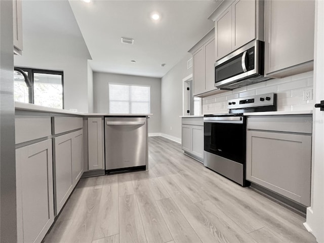 kitchen with light hardwood / wood-style flooring, appliances with stainless steel finishes, gray cabinetry, tasteful backsplash, and a healthy amount of sunlight