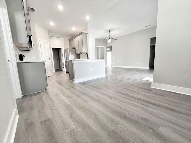 kitchen with gray cabinets, stainless steel refrigerator, sink, ceiling fan, and light hardwood / wood-style flooring