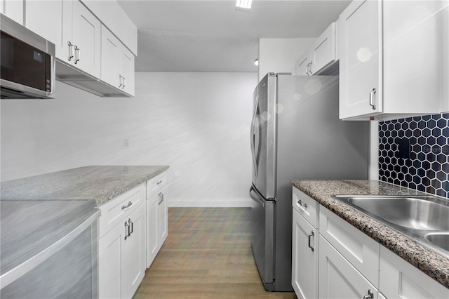 kitchen with white cabinets, tasteful backsplash, light wood-type flooring, stainless steel appliances, and light stone counters