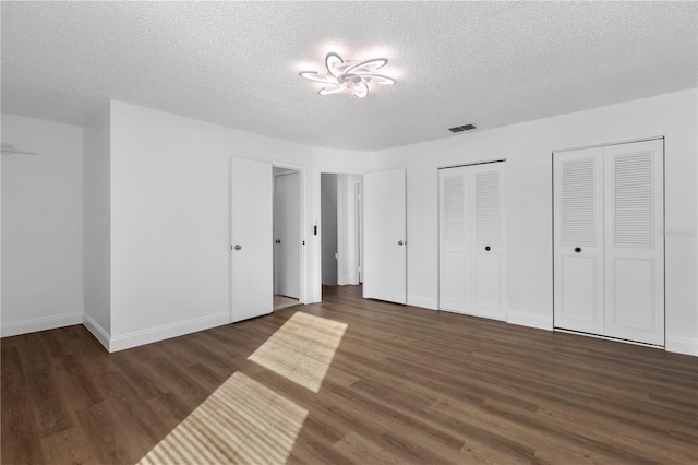 unfurnished bedroom featuring a textured ceiling, two closets, and dark hardwood / wood-style floors