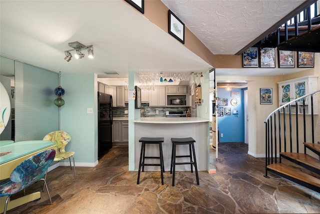 kitchen featuring a breakfast bar area, black appliances, decorative backsplash, and kitchen peninsula