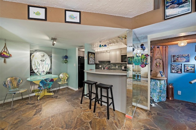 kitchen featuring a kitchen bar, decorative backsplash, black refrigerator, and kitchen peninsula