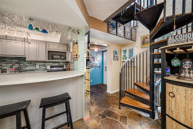 kitchen with a kitchen bar, stainless steel stove, decorative backsplash, gray cabinets, and black microwave