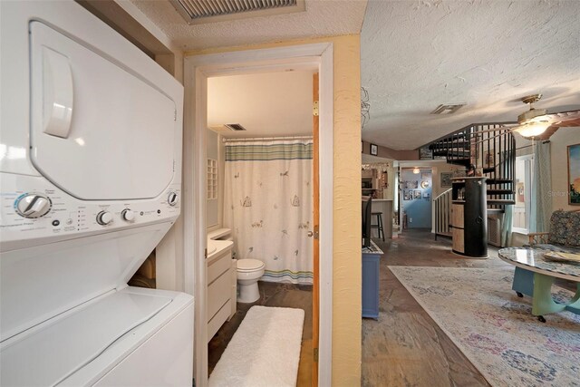 clothes washing area featuring stacked washing maching and dryer, hardwood / wood-style flooring, a textured ceiling, and ceiling fan