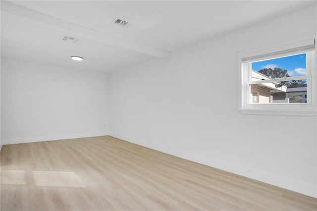 empty room with light wood-type flooring and beam ceiling