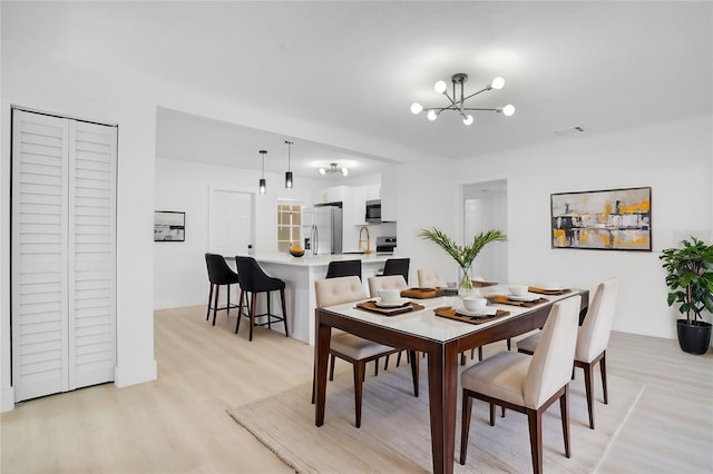 dining space with sink, light wood-type flooring, and a chandelier