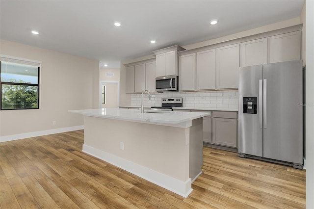 kitchen featuring a center island with sink, sink, gray cabinets, stainless steel appliances, and light hardwood / wood-style floors