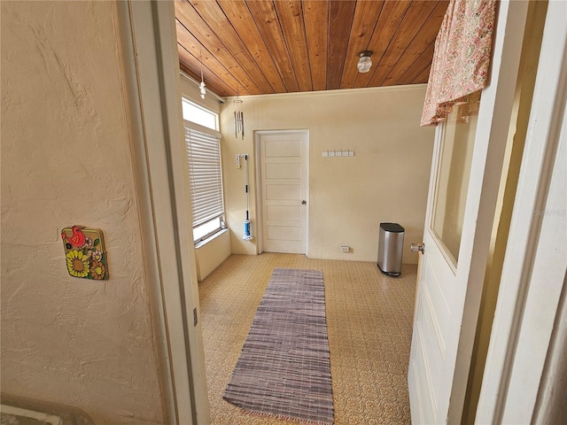 corridor with wood ceiling, ornamental molding, light colored carpet, and a wealth of natural light