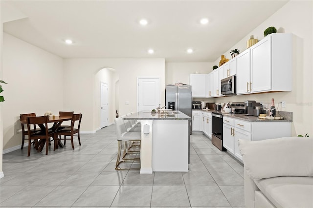 kitchen with an island with sink, stainless steel appliances, a kitchen bar, white cabinetry, and light stone counters