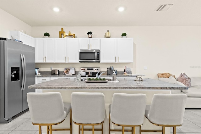 kitchen with white cabinets, stainless steel appliances, a kitchen bar, and an island with sink