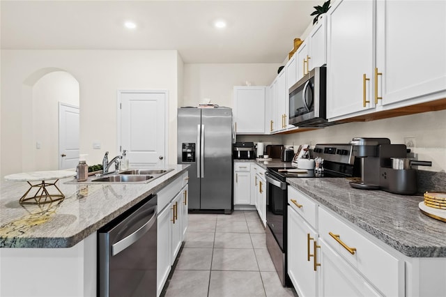 kitchen featuring white cabinets, a center island with sink, appliances with stainless steel finishes, light stone countertops, and sink