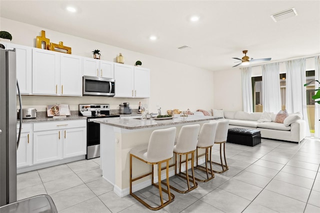 kitchen featuring white cabinets, appliances with stainless steel finishes, a kitchen island with sink, a kitchen bar, and light stone counters