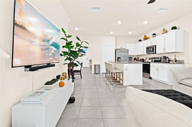 kitchen with white cabinets, light tile patterned floors, a kitchen breakfast bar, stainless steel appliances, and a center island