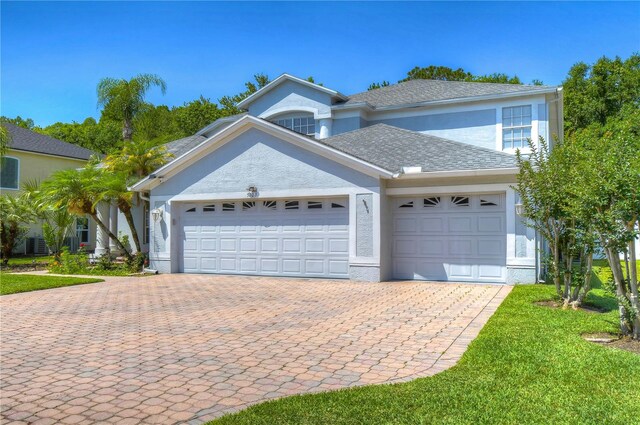 view of front of property featuring an attached garage, cooling unit, a shingled roof, decorative driveway, and stucco siding