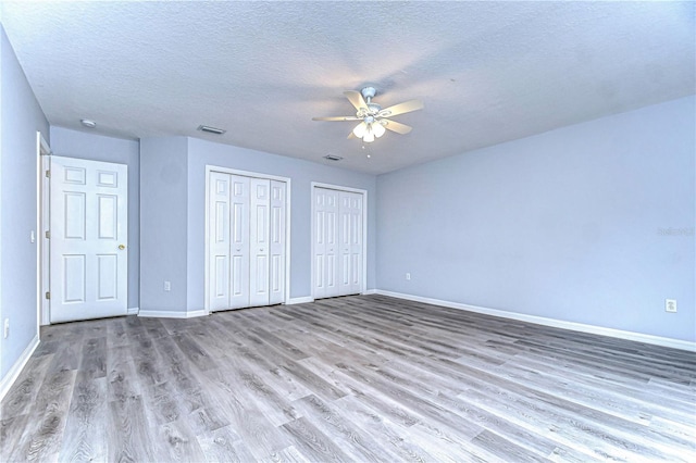 unfurnished bedroom with multiple closets, visible vents, a textured ceiling, light wood-type flooring, and baseboards