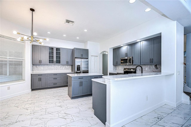 kitchen with pendant lighting, marble finish floor, stainless steel appliances, glass insert cabinets, and a peninsula