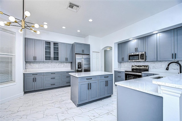 kitchen featuring marble finish floor, stainless steel appliances, visible vents, hanging light fixtures, and glass insert cabinets