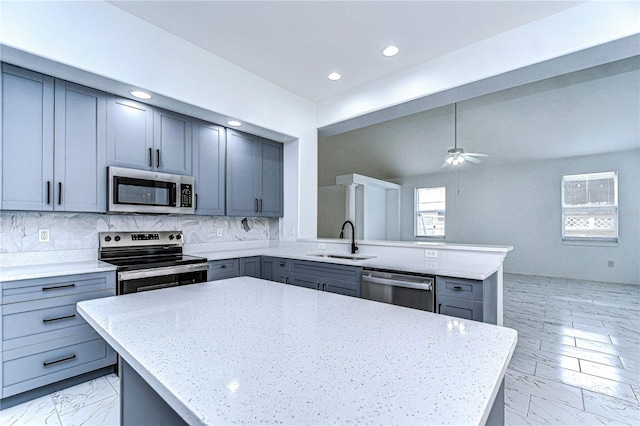 kitchen with light stone counters, stainless steel appliances, a peninsula, a kitchen island, and a sink