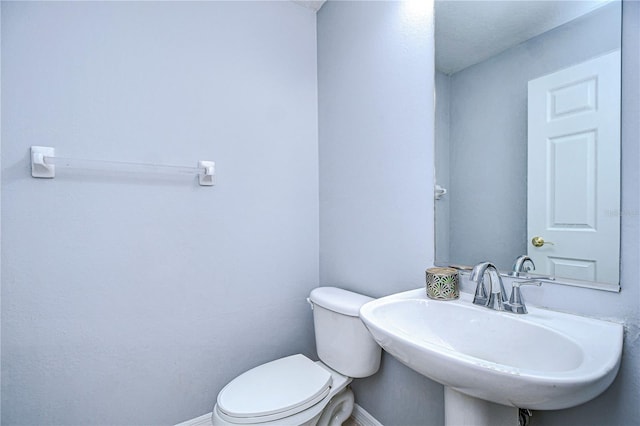 half bath with toilet, baseboards, and a sink