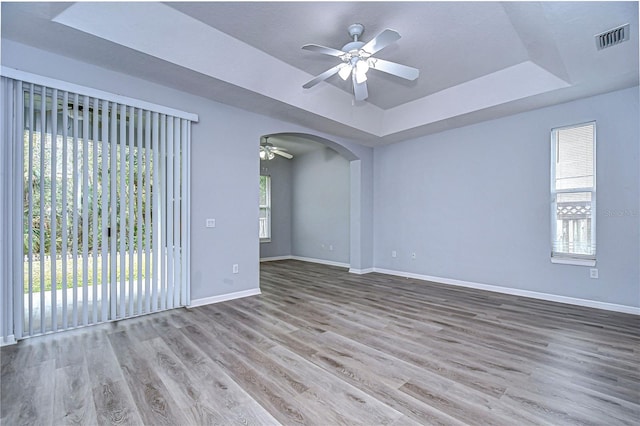 empty room with arched walkways, a raised ceiling, visible vents, light wood-style floors, and baseboards