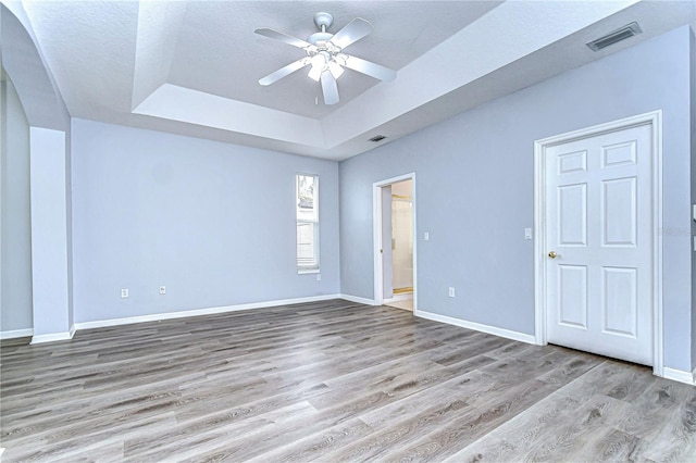 empty room featuring baseboards, visible vents, a ceiling fan, a tray ceiling, and light wood-type flooring